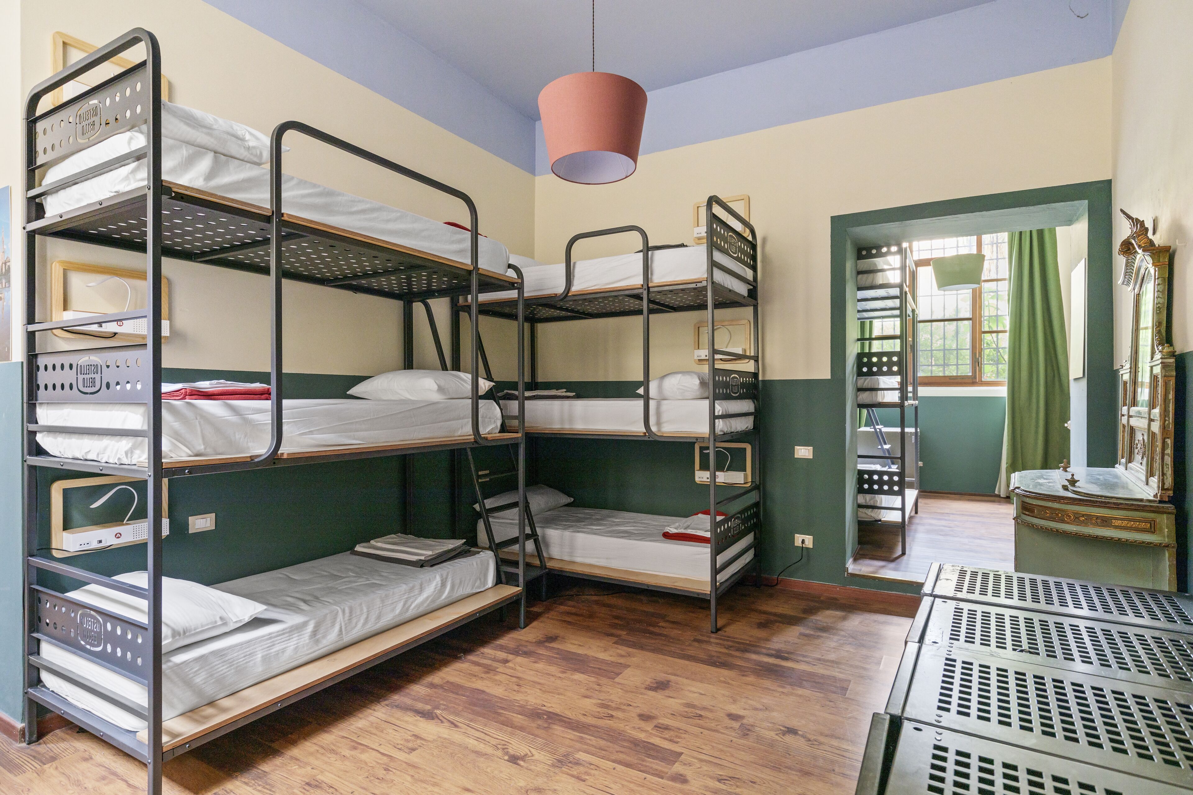 Une chambre avec un lit superposé, un plancher en bois, un luminaire suspendu et une porte donnant sur une autre pièce.