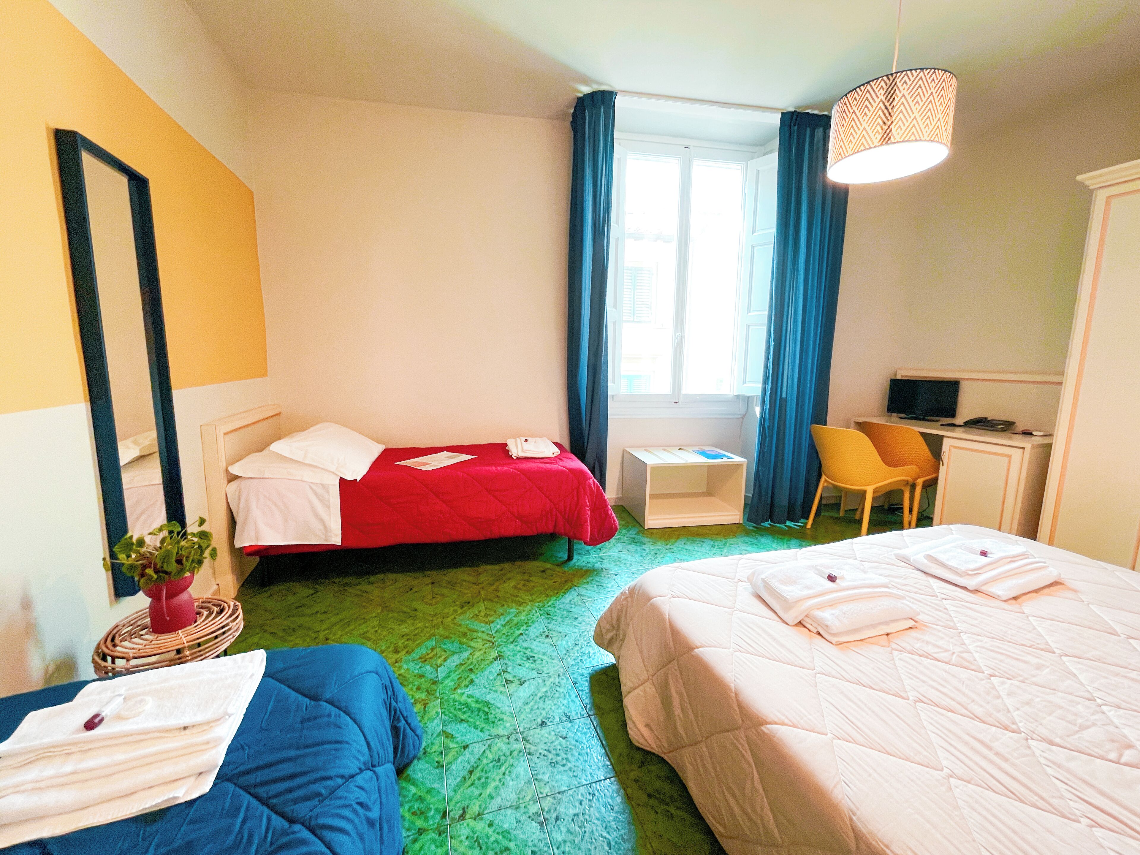 A hotel room with two beds, a desk with a computer, a chair, and a window with curtains.