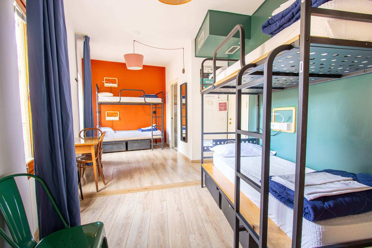 Un dormitorio con literas, escritorio, sillas y ventana con cortinas.