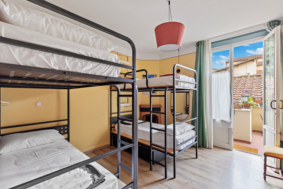 Une chambre de dortoir avec des lits superposés, une lampe suspendue rouge et une porte-fenêtre coulissante donnant sur un balcon extérieur.