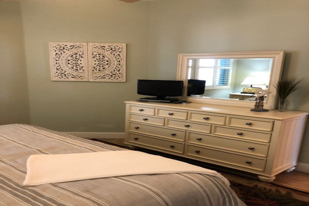 A bedroom with a bed, a dresser, a television, and two wall art pieces.