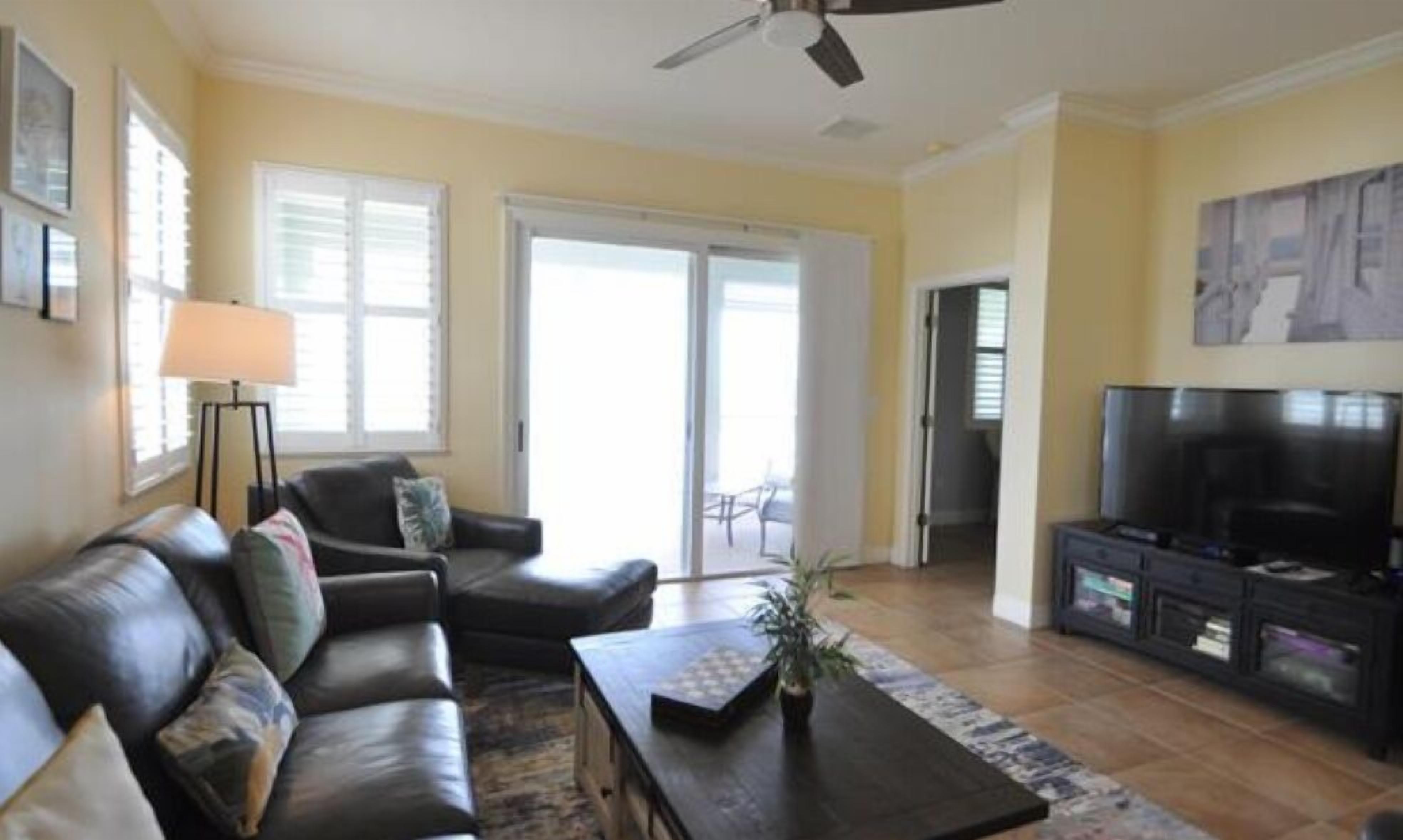 A living room with a sofa, coffee table, TV, and a ceiling fan.