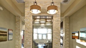 A lobby with a stone wall, two chandeliers, and a reception desk.