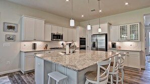 A modern kitchen with white cabinetry, granite countertops, stainless steel appliances, and pendant lighting.