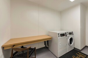 A laundry room with a wooden desk, a chair, and a front-loading washing machine.