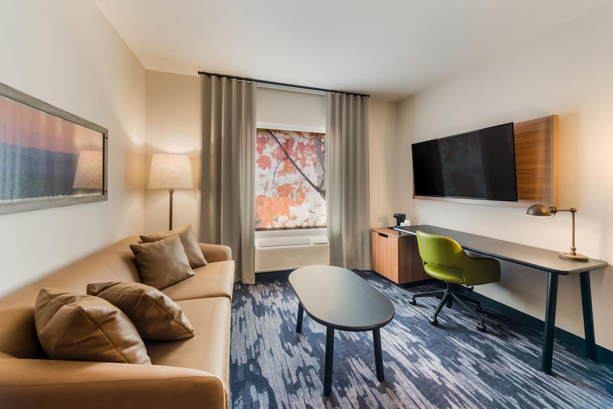 Een hotelkamer met een bank, een bureau, een stoel, een flatscreen televisie en een raam met gordijnen.