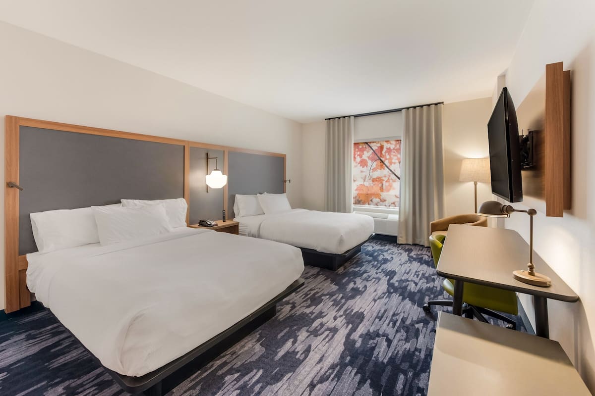 Hotelkamer met twee bedden, een bureau, een stoel, een televisie en een raam met gordijnen.