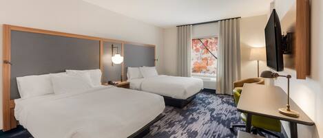 A hotel room with two beds, a desk, a chair, a TV, and a window with curtains.