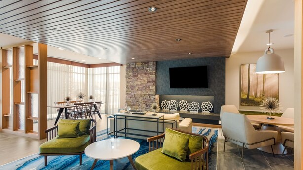 A modern living room with a stone accent wall, a flat-screen TV, and a dining area with a glass table and chairs. - Fairfield Inn & Suites by Marriott Columbus Canal Winchester (Canal Winchester)