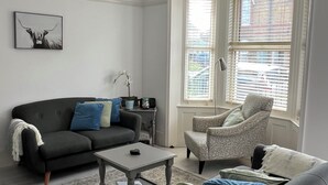 A living room with a dark grey sofa, a patterned armchair, a coffee table, and a chandelier.