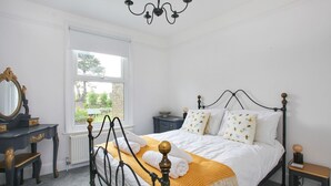 A bedroom with a bed, a dresser, a nightstand, a mirror, and a window with a view of greenery.