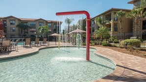 A pool area with a water feature, surrounded by buildings with balconies and palm trees.
