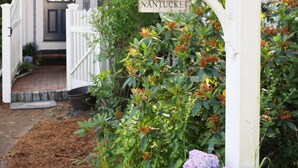 Een huis met een witte hekken, een bordje met de tekst 'NANTUCKET' en een tuin met hortensia's.