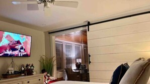 Een slaapkamer met een bed, een televisie, een bureau en een schuifdeur naar een balkon.