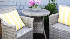 Een terras met rieten meubels en een tafel, voor een gebouw met witte sierlijsten en blauwe bekleding.