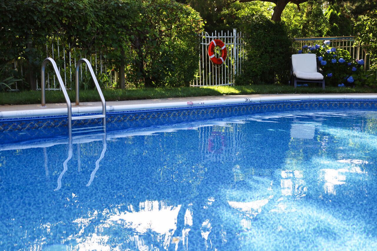 Una piscina con escaleras de metal, una silla blanca y una cerca con un salvavidas.