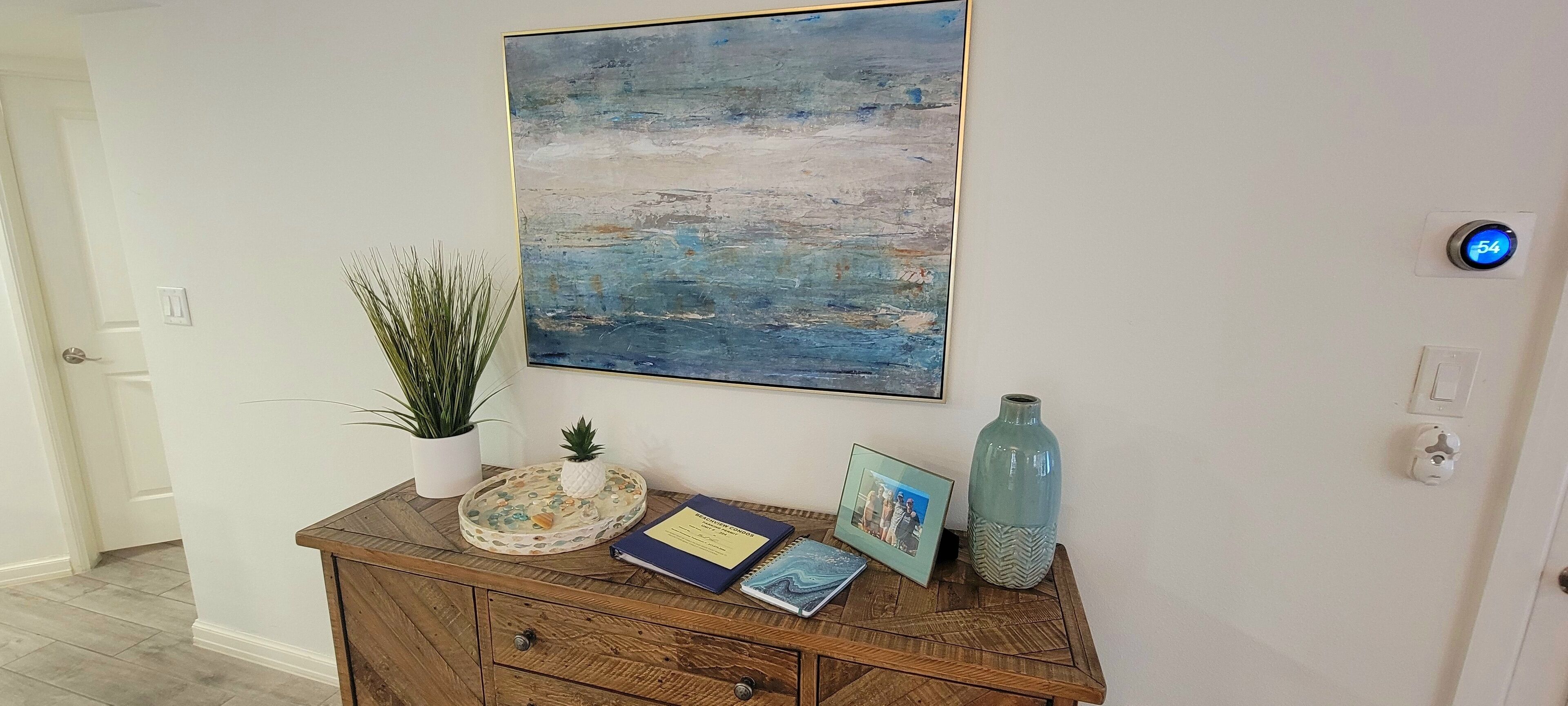 A wooden console table with a decorative tray, a framed photo, a blue notebook, and a potted plant.