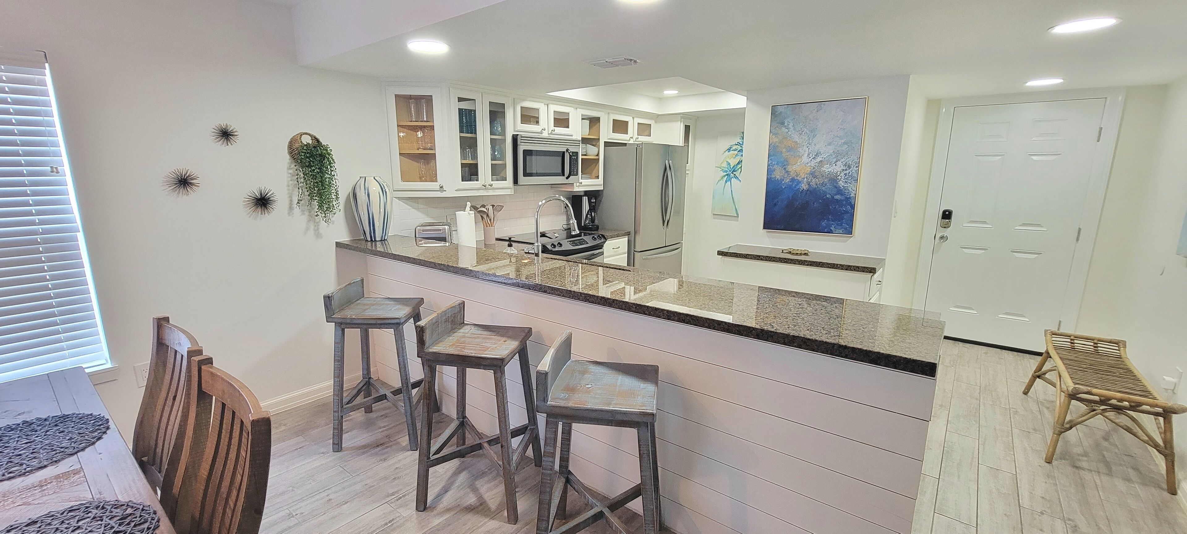 A modern kitchen with a central island, bar stools, and a dining area with a wooden table and chairs.