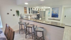 Cozinha moderna com ilha central, banquetas e área de jantar com mesa e cadeiras de madeira.