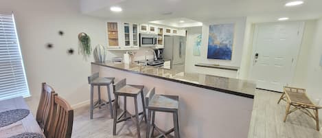 A modern kitchen with a central island, bar stools, and a dining area with a wooden table and chairs.