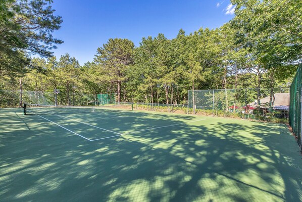Una cancha de tenis al aire libre rodeada de árboles.