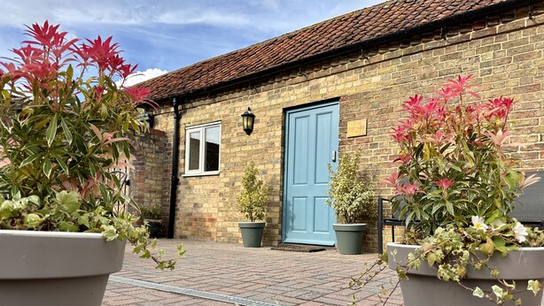 A brick cottage with a blue door, potted plants, and a brick pathway.