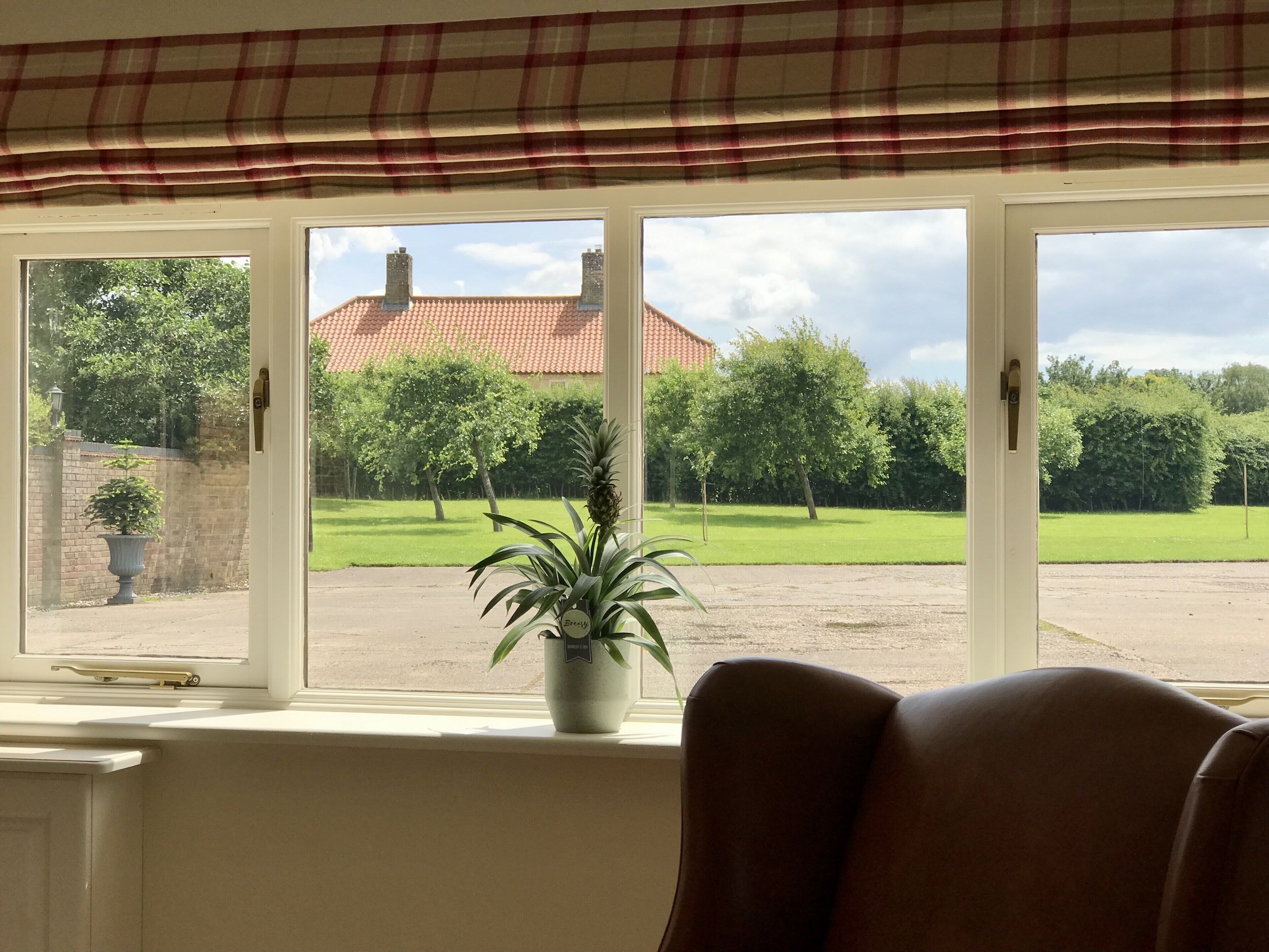 Ein Zimmer mit großem Fenster mit Blick auf eine grüne Wiese und ein Gebäude mit rotem Dach.
