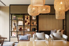 A modern interior with a wooden dining table, two sofas with cushions, a bookshelf, and woven pendant lights. - Fairfield by Marriott Gifu Takayama Shirakawa Go (Takayama)