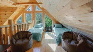 A wooden cabin with two beds and bean bags, large windows, and a balcony.