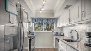 Une cuisine moderne dotée d’appareils électroménagers en acier inoxydable, de meubles blancs et d’une fenêtre agrémentée d’un lambrequin à motifs.