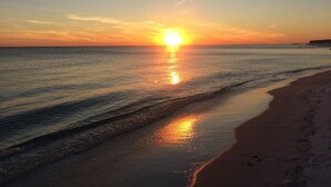 Une plage où l’on peut admirer le coucher de soleil sur l’océan, une rive sablonneuse et des empreintes de pas dans le sable.