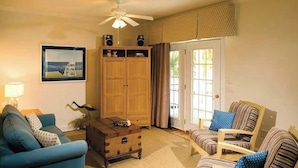 Un salon avec un canapé bleu, un meuble en bois, une chaise en bois et un ventilateur de plafond.