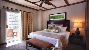 Une chambre d’hôtel avec un lit, un ventilateur de plafond, une fenêtre avec des rideaux, un tableau encadré au mur et une lampe de chevet.