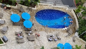 Une piscine entourée de chaises longues et de parasols, où des gens nagent et se détendent.