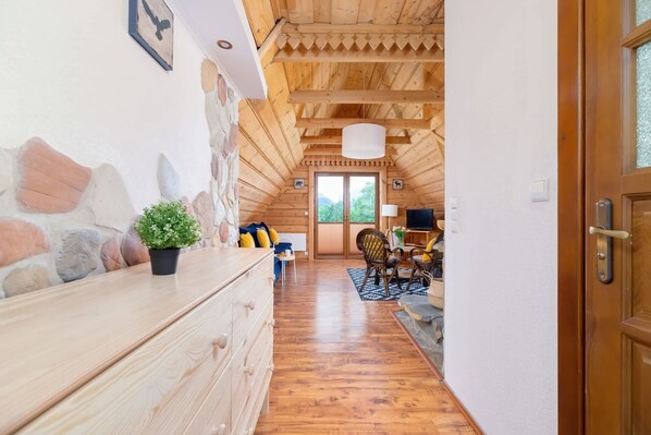 Un interior de madera con una pared de piedra, un tocador de madera, una planta en maceta, una silla, un televisor y una puerta.