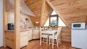 Una cabaña de madera acogedora con una zona de cocina que incluye una mesa de comedor, sillas, un microondas y un refrigerador.