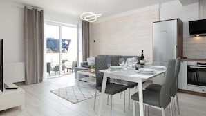 A modern kitchen with a built-in refrigerator, a dining table set for four, and a large window overlooking a residential area. - Modern Apartment close to the Beach | Balcony | Parking (Darlowo)