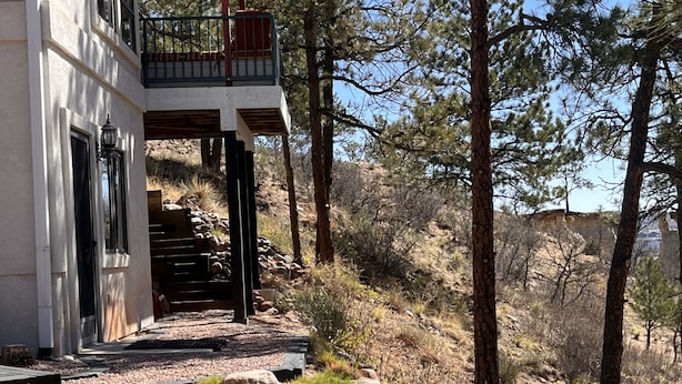 A modern house with a balcony, a stone staircase, and a surrounding natural landscape.