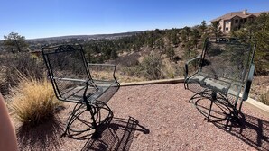 Two metal chairs on a gravel patio with a view of a residential area and hills in the background.