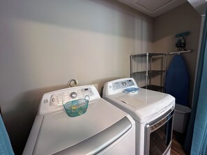 A laundry area with two front-loading washing machines and a metal shelf unit.