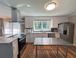 A kitchen with a central island, a microwave, a refrigerator, and a window with a view of greenery.