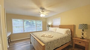 A bedroom with a wooden bed, a ceiling fan, a bedside table with a lamp, and a window with blinds. - Cozy Lake Hartwell Cottage near Tugaloo State Park (Lavonia)