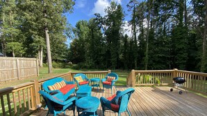 A wooden deck with blue wicker furniture, a barbecue grill, and a view of a wooded area. - Cozy Lake Hartwell Cottage near Tugaloo State Park (Lavonia)