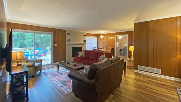 A spacious living room with a fireplace, a red sofa, a coffee table, and a dining area with chairs. - Cozy Lake Hartwell Cottage near Tugaloo State Park (Lavonia)
