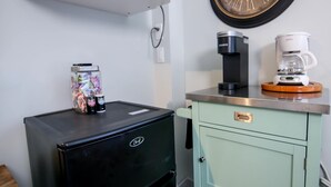 Una piccola cucina accessoriata con un frigorifero nero, una macchina del caffè e una sveglia appesa al muro.