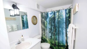 Un bagno con lavandino, water e tenda da doccia a tema foresta.