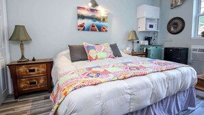 Una camera da letto con un letto grande, un comodino con cassetti, una lampada, un quadro appeso al muro, una sveglia e una finestra con tende.
