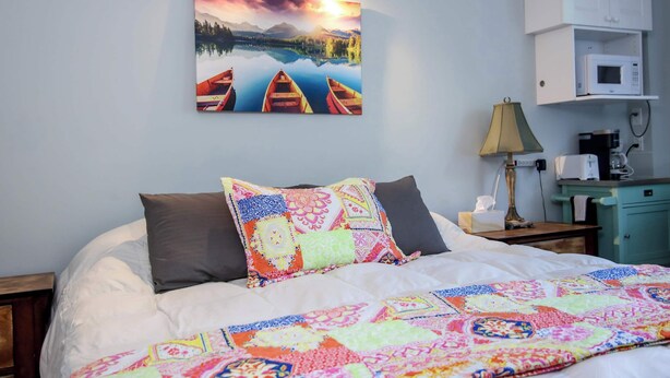 Un letto rifatto con una coperta colorata, un quadro che raffigura canoe su un lago, una lampada e un forno a microonde su un mobiletto.