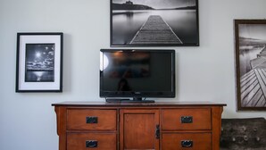 Un televisore su un mobile in legno con tre cassetti, circondato da quadri appesi al muro.