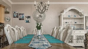 Comedor con mesa de madera, sillas blancas, una araña y un aparador decorativo.